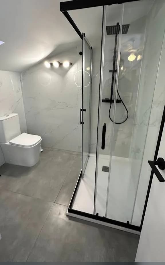 Bathroom with a black-framed glass shower enclosure, rainfall shower, white tray, marble-effect walls and grey tiled floor. Source: Avilan M
