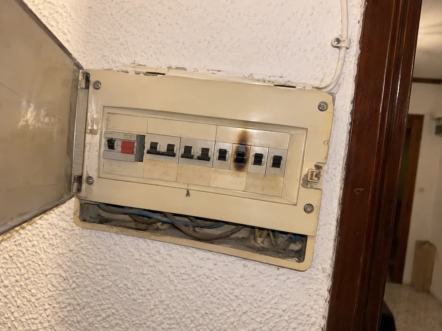 The old fuse board in the hallway, scorched around one breaker, cables loose underneath
