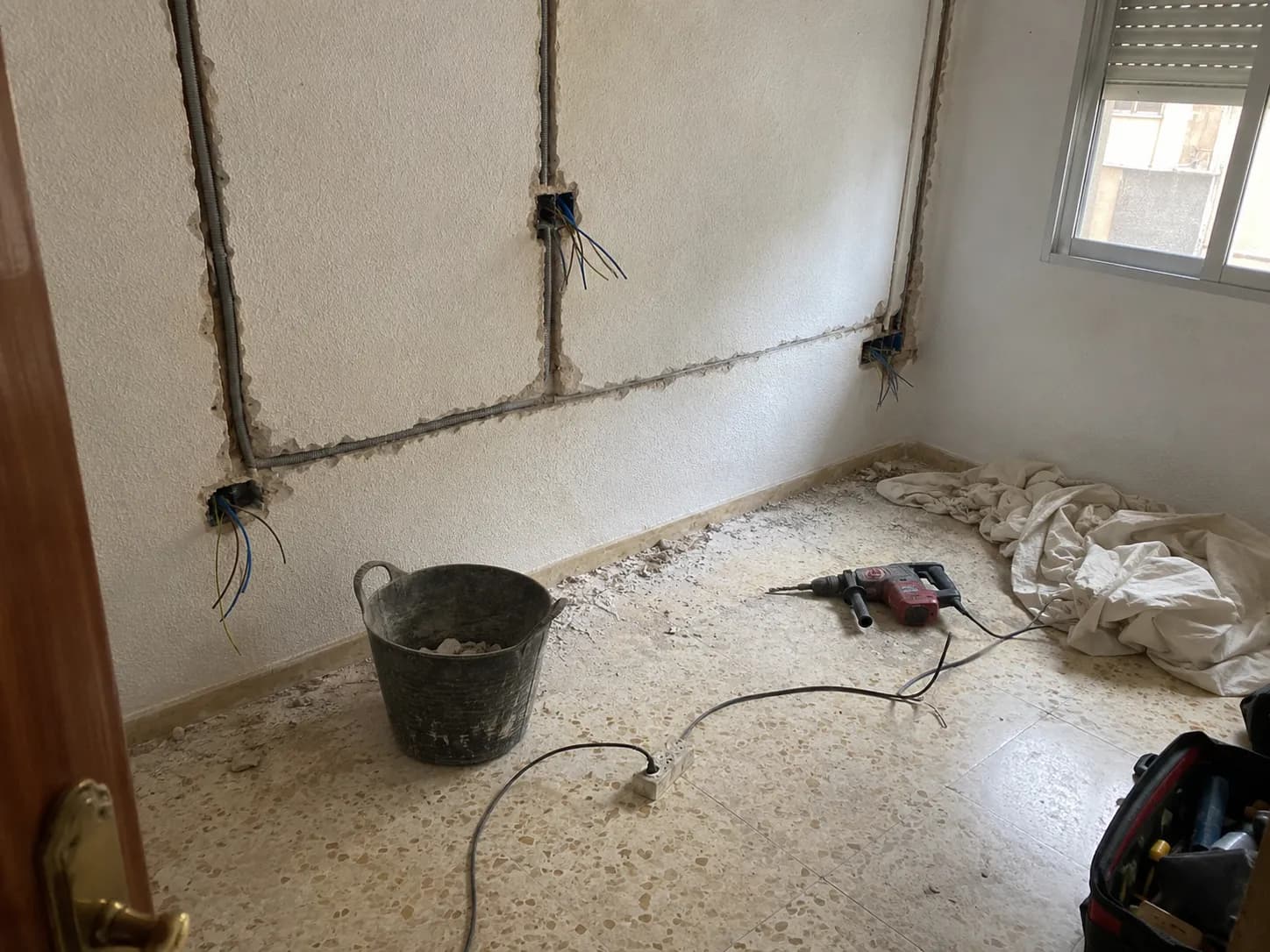 Bedroom mid-rewire: walls chased, new conduit in, cable ends out of the socket boxes