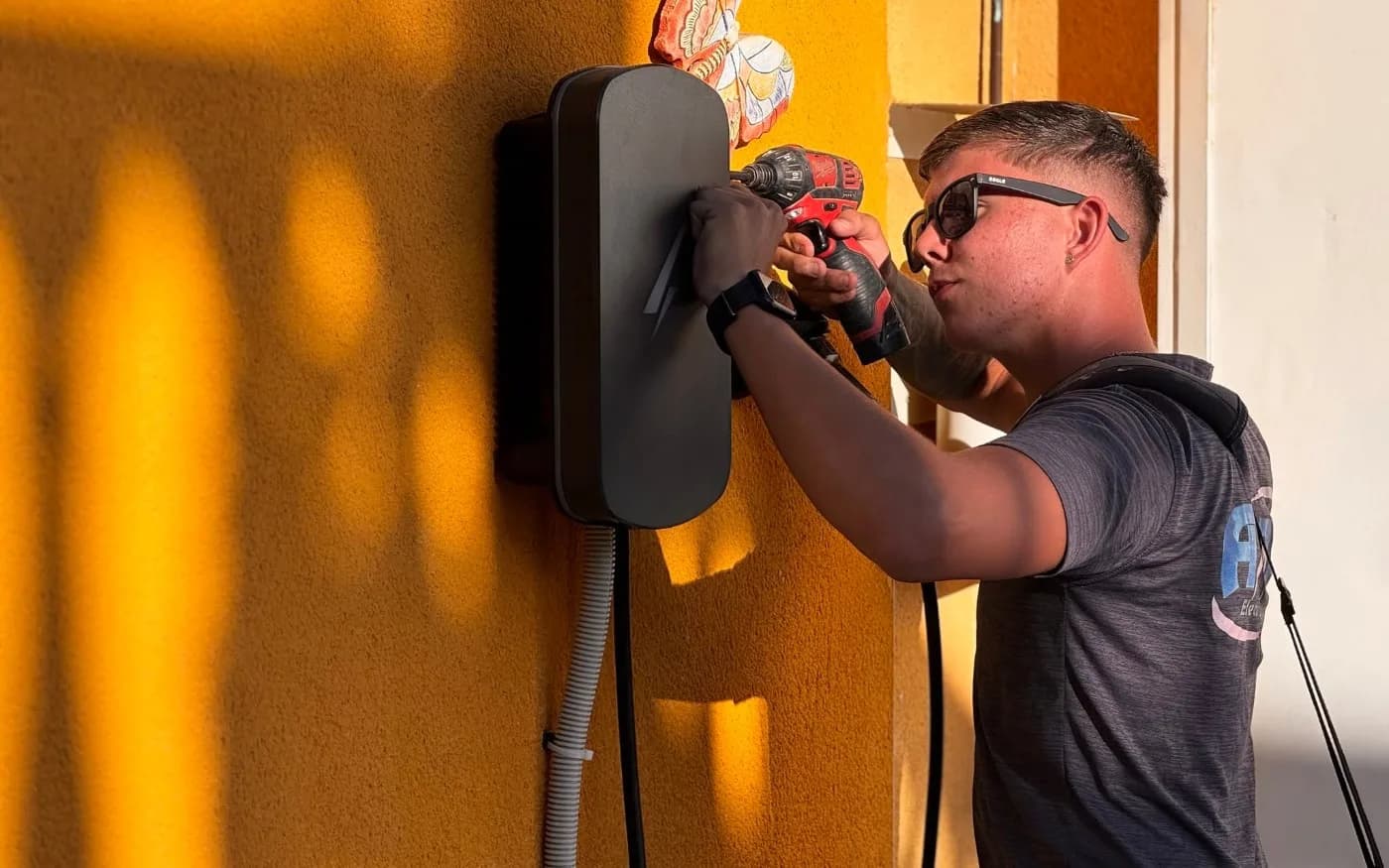 Wall-mounted EV charger being secured, with cabling run in conduit below.