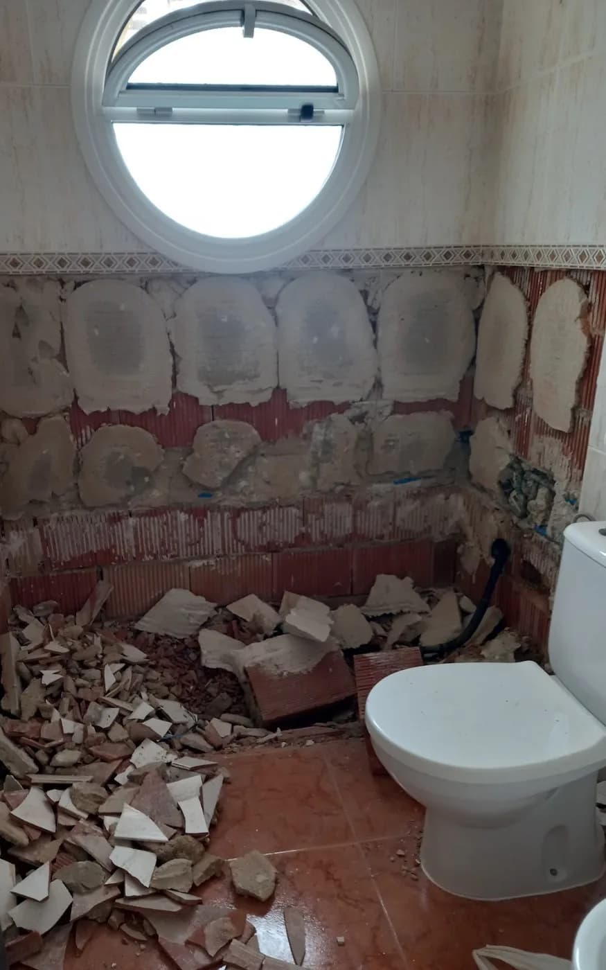 Lower wall tiles removed during preparation for the shower, with the round window and existing toilet retained.