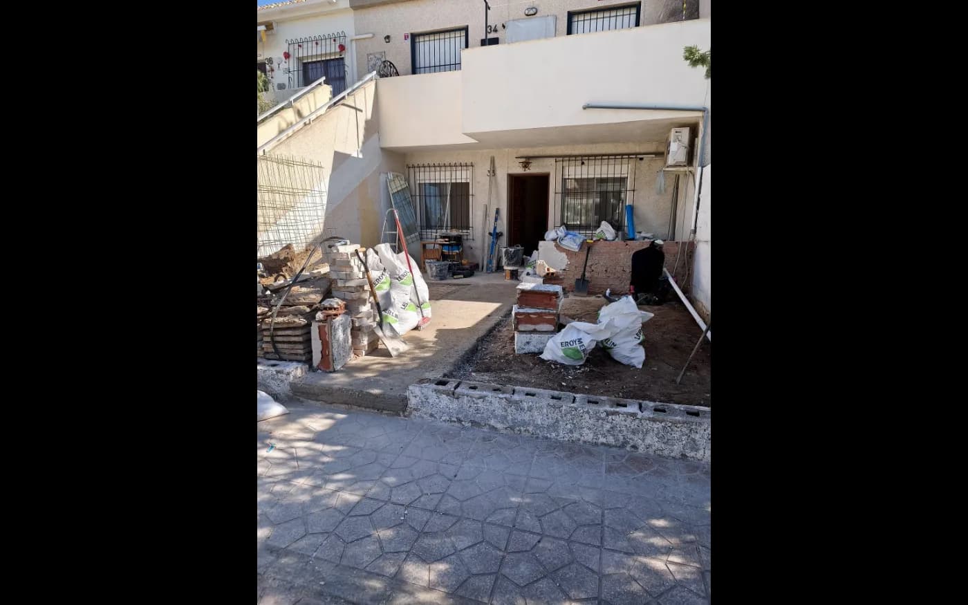 Front terrace during renovation, with sections of old paving removed and building materials on site.